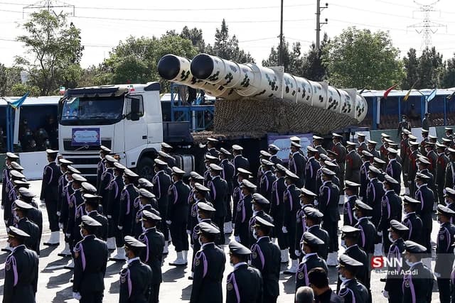Iranian military personnel in uniform during a parade with a missile system on a truck.
