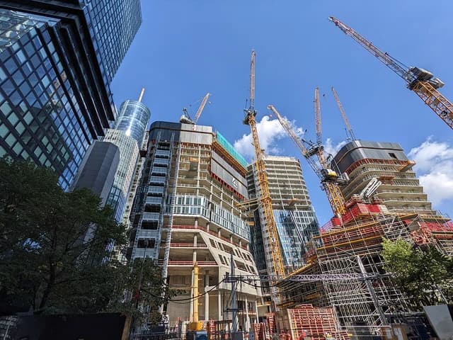 Skyscrapers under construction with multiple cranes in Frankfurt, Germany, against a blue sky.