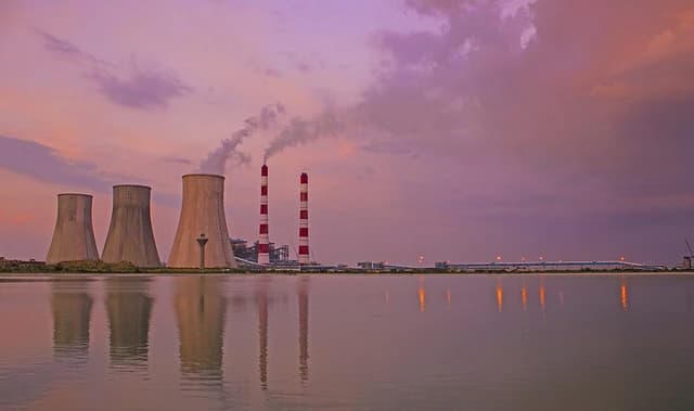 Haryana Thermal Power Plant with cooling towers, smokestacks, and water in foreground at dusk.