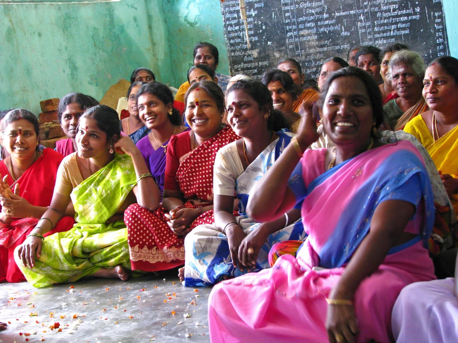 Many rural Indian women sitting on the floor, smiling and looking forward.