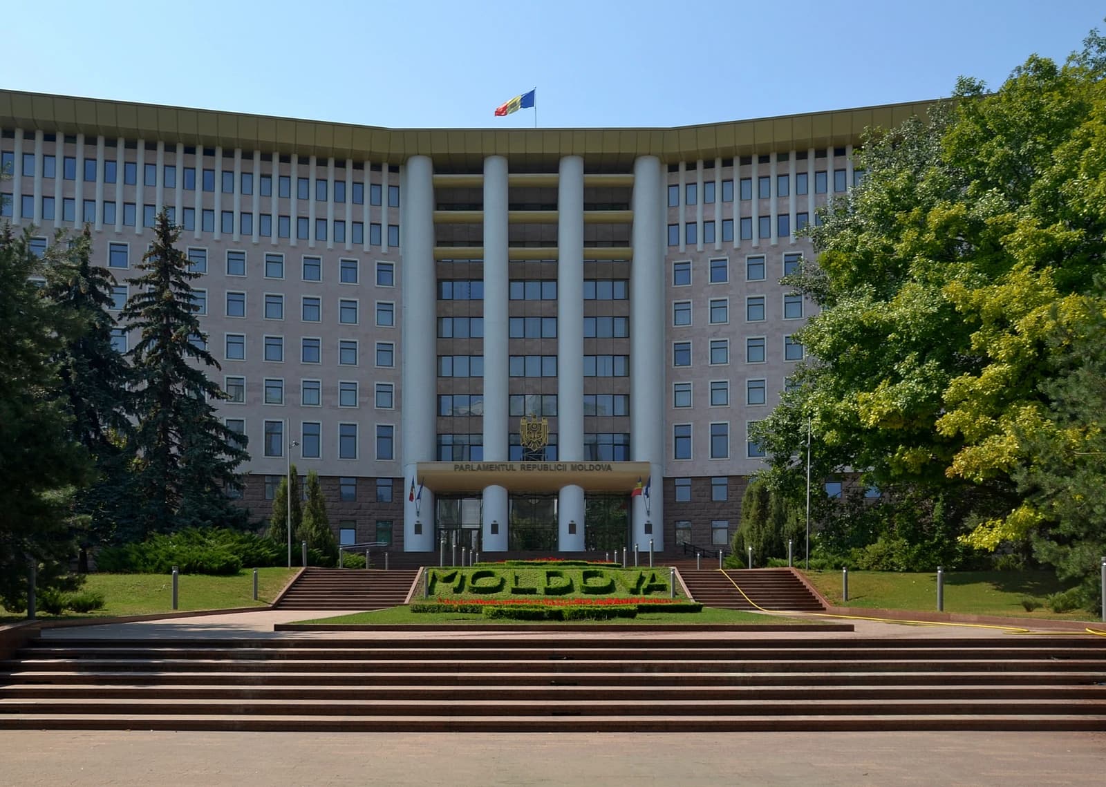Parliament Building in Chișinău, Moldova, with a flowerbed spelling 'MOLDOVA' in front.