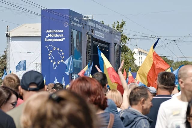 Crowd of people attending "Moldova Europeană" assembly, waving national and EU flags.