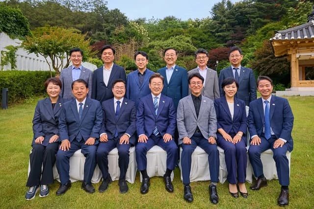 Lee Jae-myung seated with Democratic Party of Korea lawmakers for a group photo outdoors.