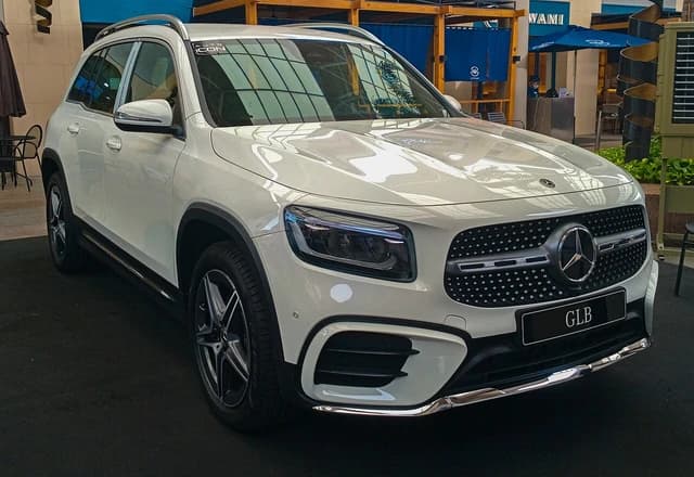 White 2024 Mercedes-Benz GLB 200 AMG Line SUV parked indoors, showing front grille and headlights.