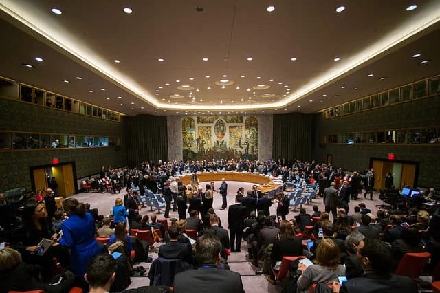 People stand and sit in the United Nations Security Council Chamber before a meeting.
