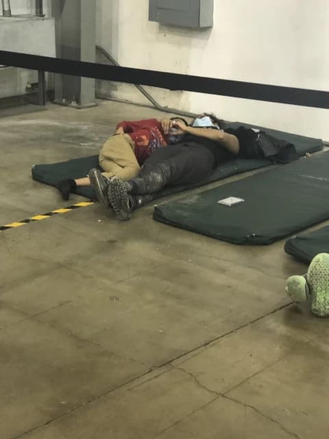 Two people lying on green mats on a concrete floor in an indoor facility.