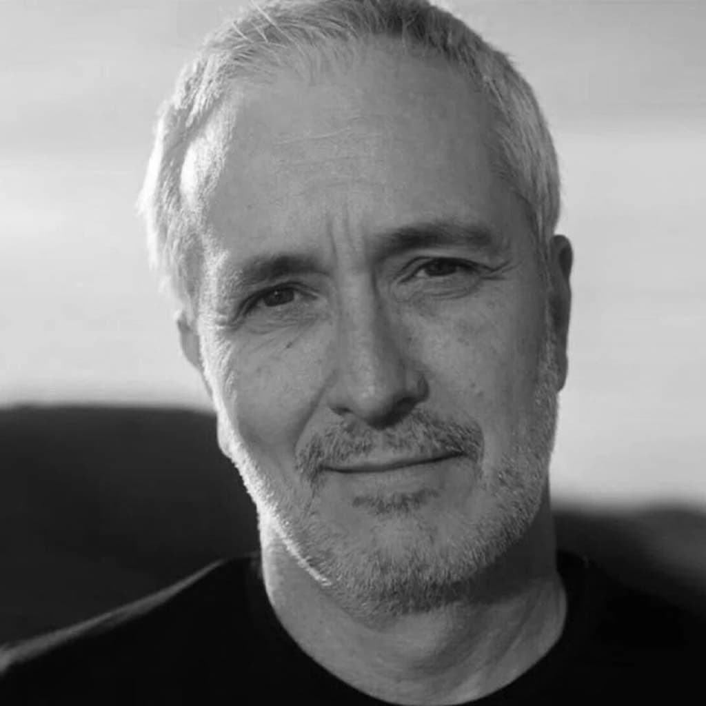Andre Vellozo, a man with grey hair and beard, looks towards the viewer.