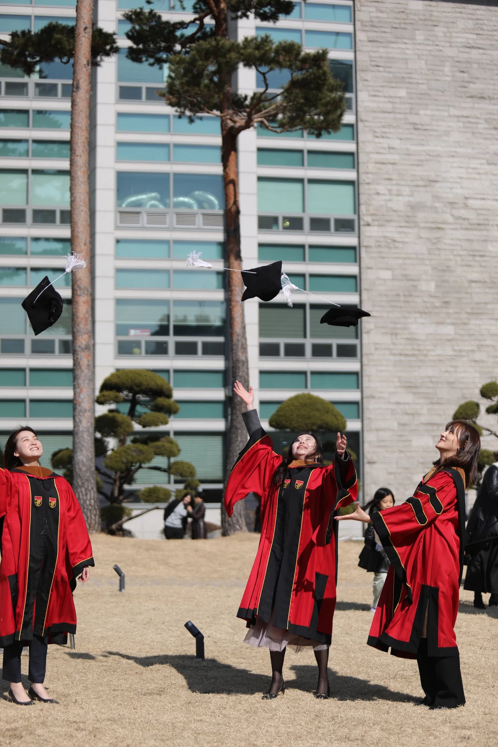 Three graduates in red and black academic gowns throwing their caps into the air.