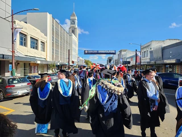 Massey University graduates walk in a procession through a city street in academic gowns.