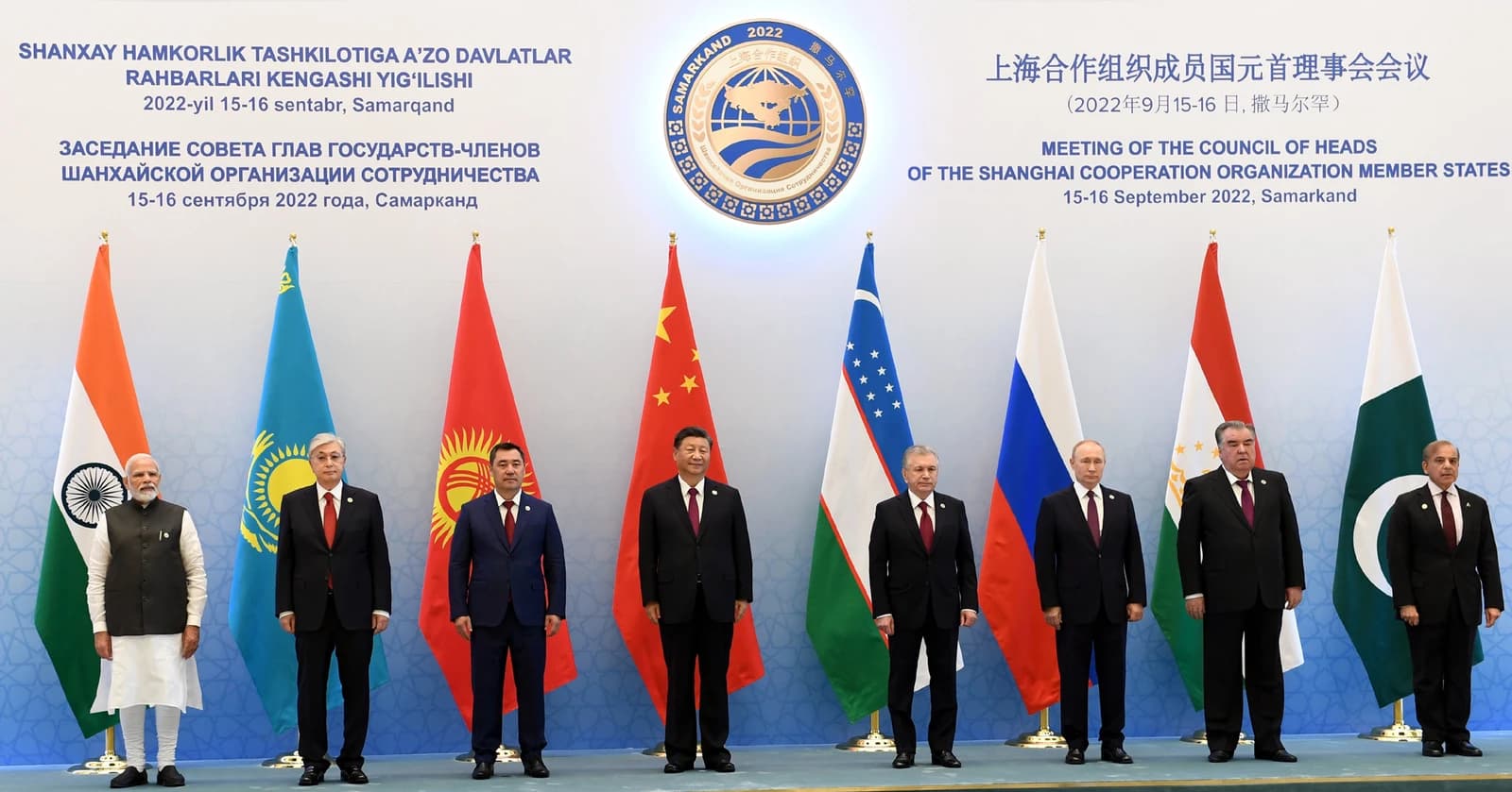 Leaders from various nations stand in a line in front of their national flags.