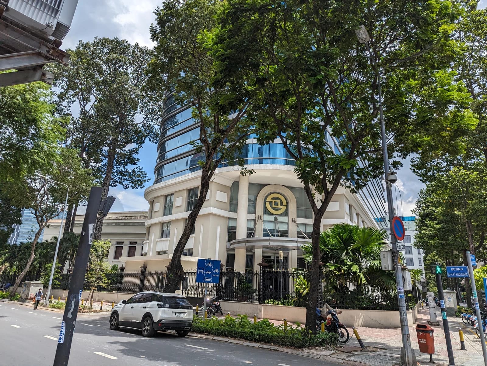 Building with a circular logo on its facade on a tree-lined street in Saigon.