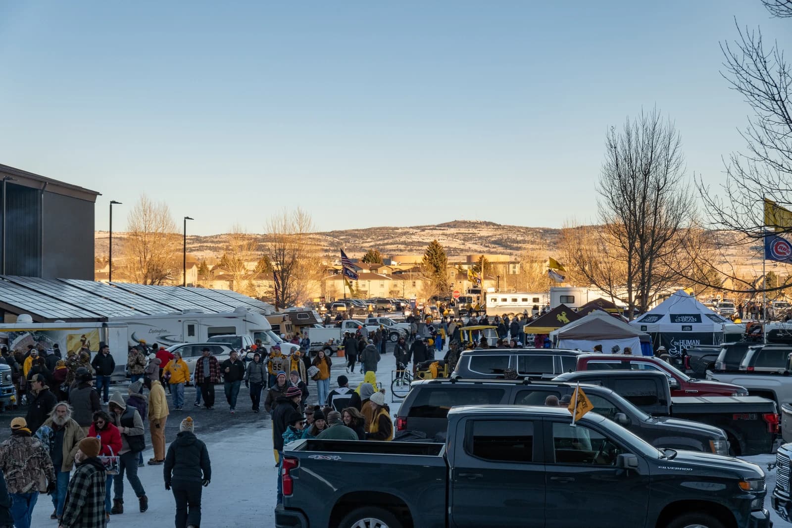 People walk through a parking lot filled with vehicles and tailgating tents before a football game.