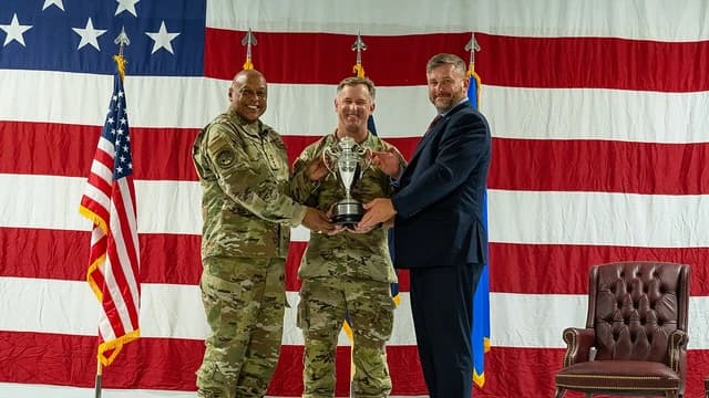 Military general, military officer, and civilian receiving a trophy.