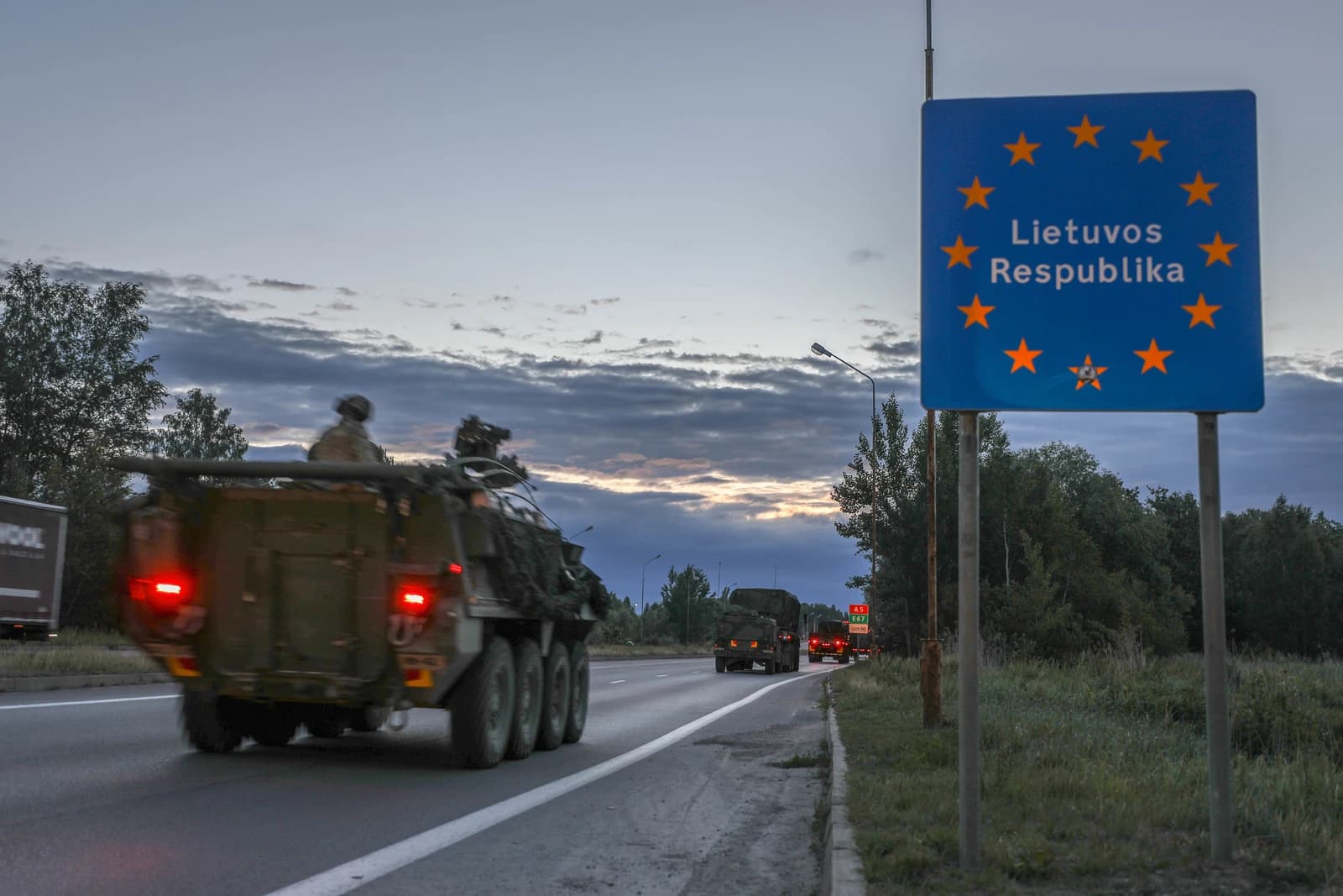 Military vehicles with soldiers entering Lithuania at a border crossing.
