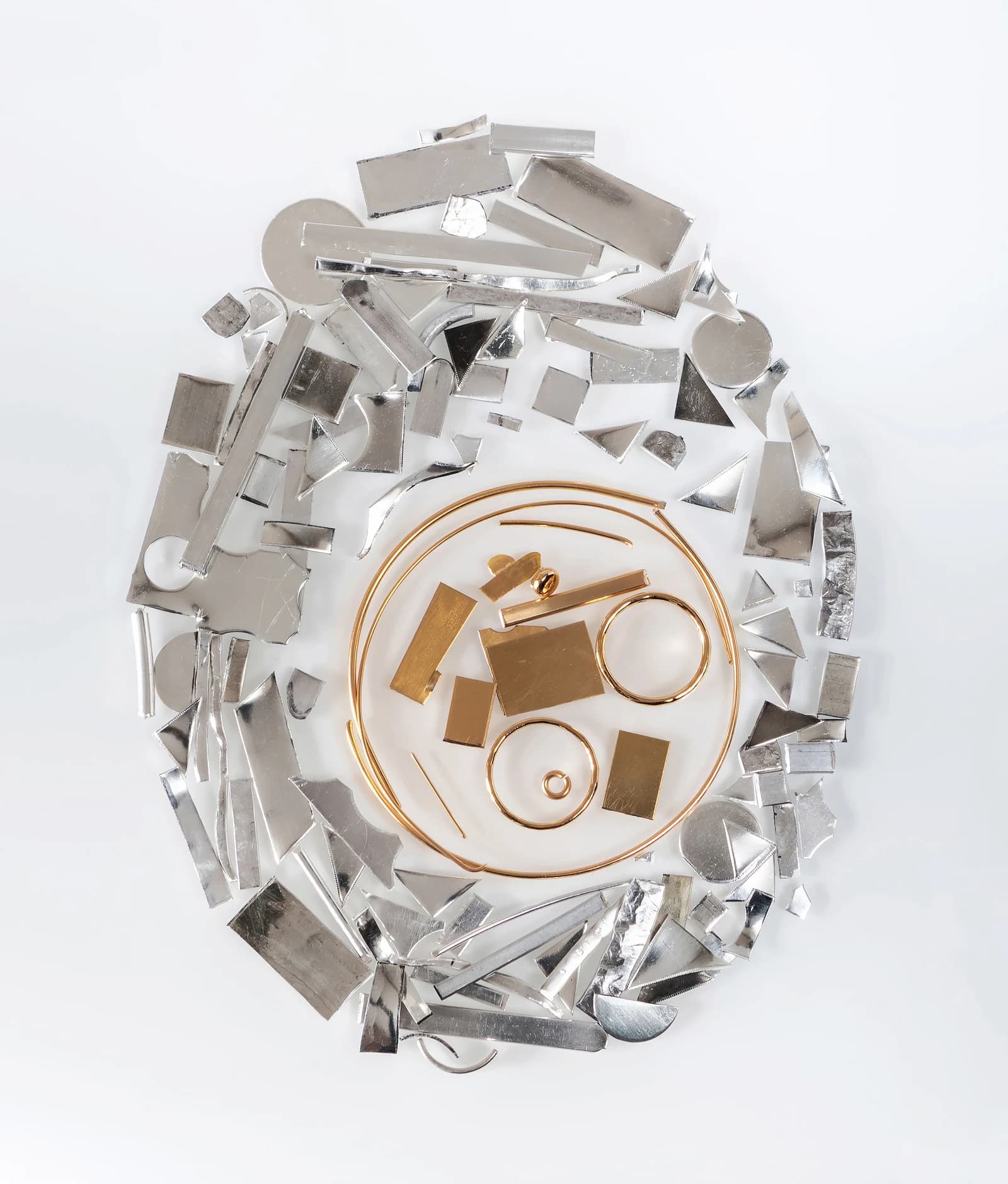 Various pieces of silver and gold scrap metal arranged on a white surface.