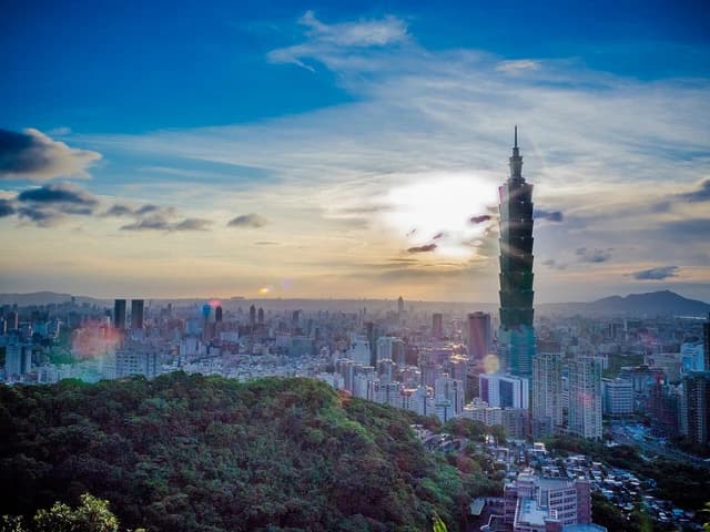 Taipei 101 skyscraper towers over the city skyline at sunset with a bright sky.