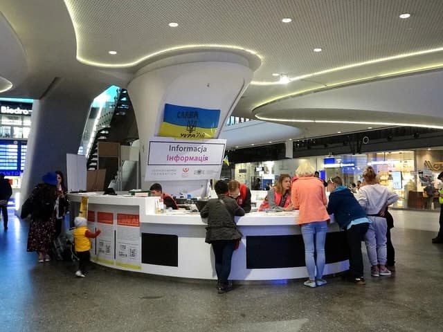 People gather around an information desk with Ukrainian flag at a Polish train station.