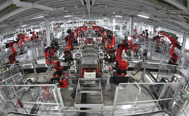 Robotic arms assemble vehicles on a Tesla Motors production line.