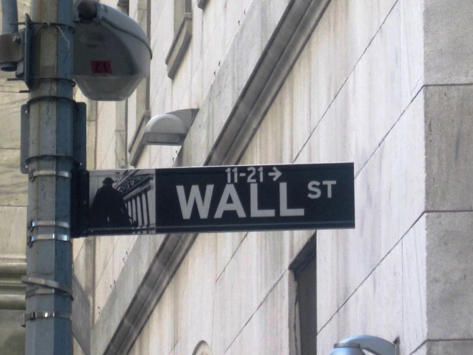 Wall Street street sign attached to a pole with a building in the background.