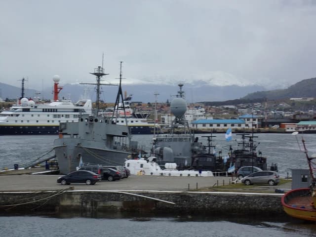 Military ships docked at Naval Base Ushuaia with snowy mountains visible in the distance.