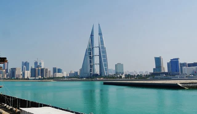 Manama skyline features the distinctive Bahrain World Trade Center towers beside blue water.