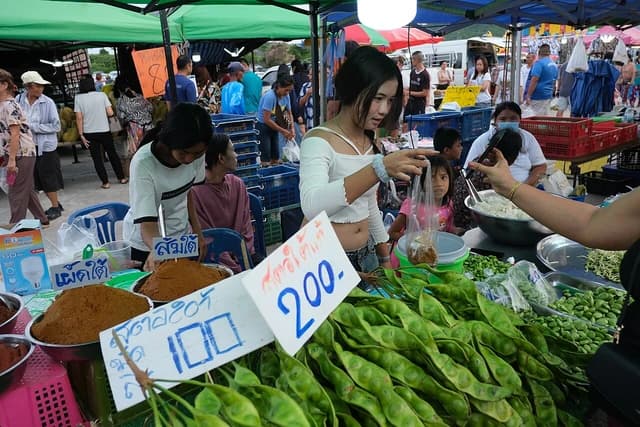 Young vendor bagging fresh produce for a shopper at a busy outdoor market stall.