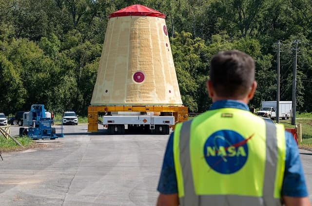 NASA employee in safety vest observing large rocket component on a trailer.