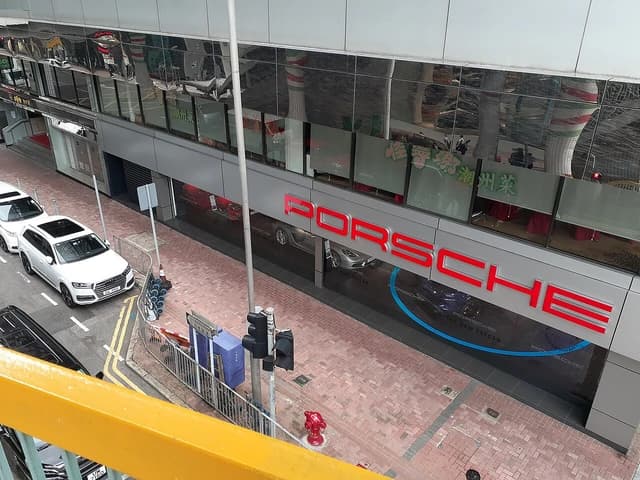 Porsche showroom with red PORSCHE lettering and parked cars on Gloucester Road, Hong Kong.