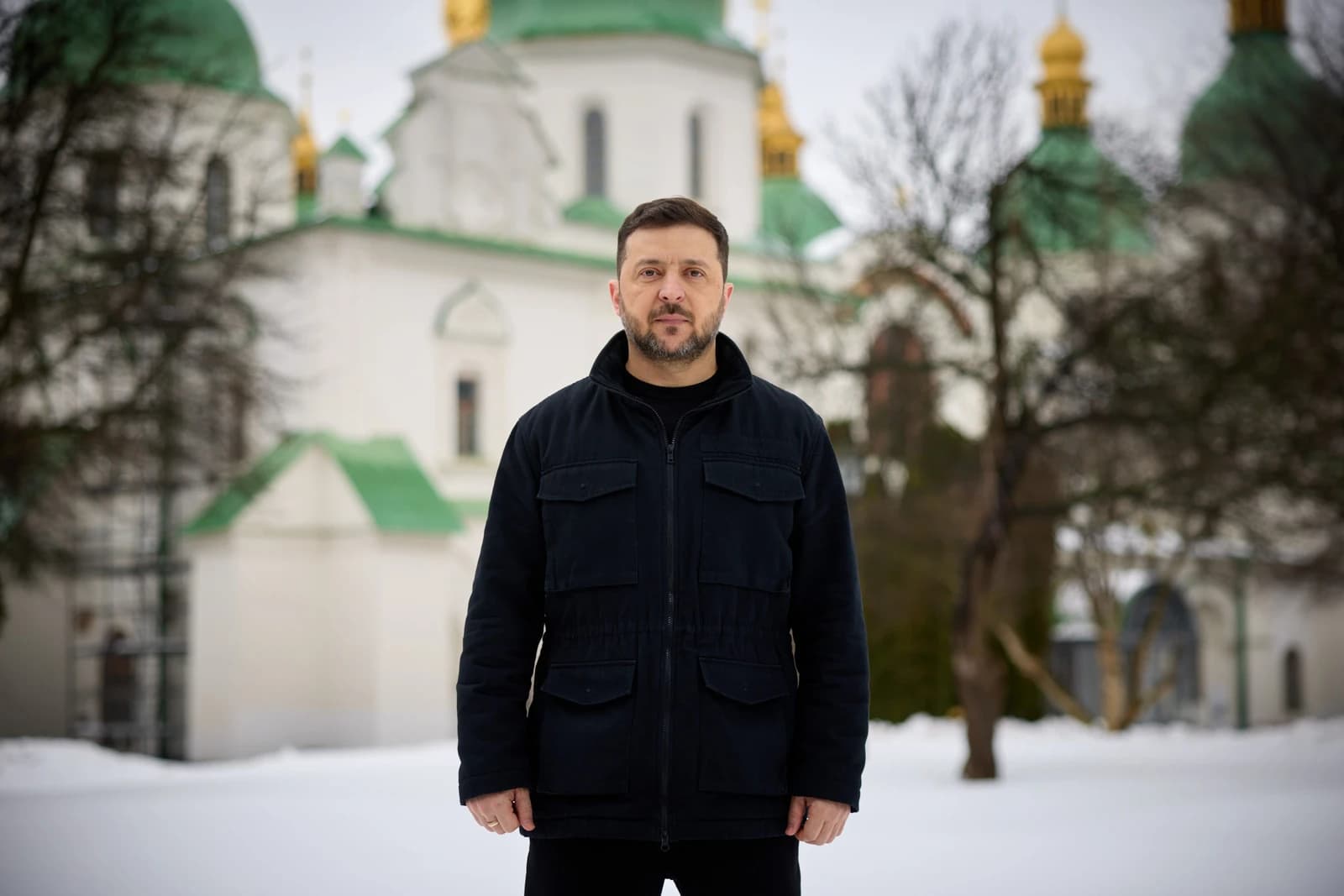 Volodymyr Zelenskyy, President of Ukraine, stands outdoors in a snowy landscape.