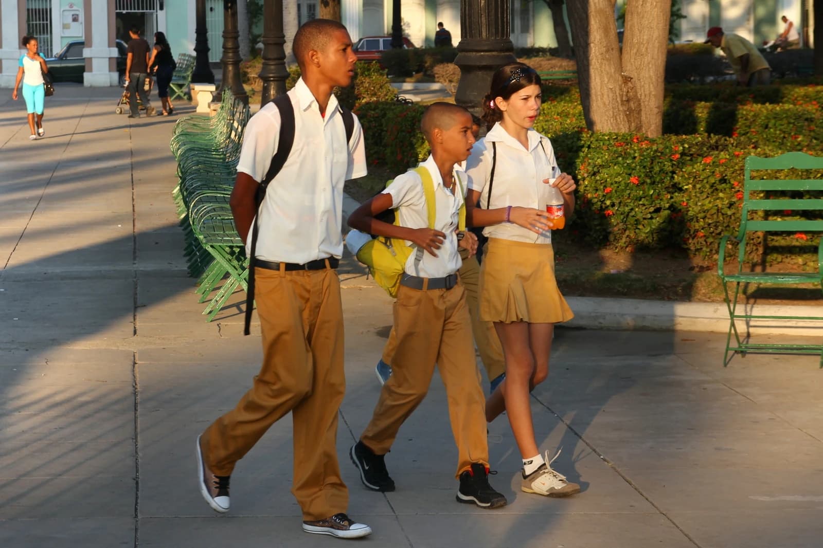 Three school children wearing uniforms walk along a sunny sidewalk in Cuba.