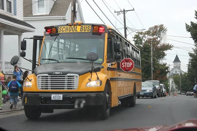 A yellow school bus is stopped on a residential street with children nearby.