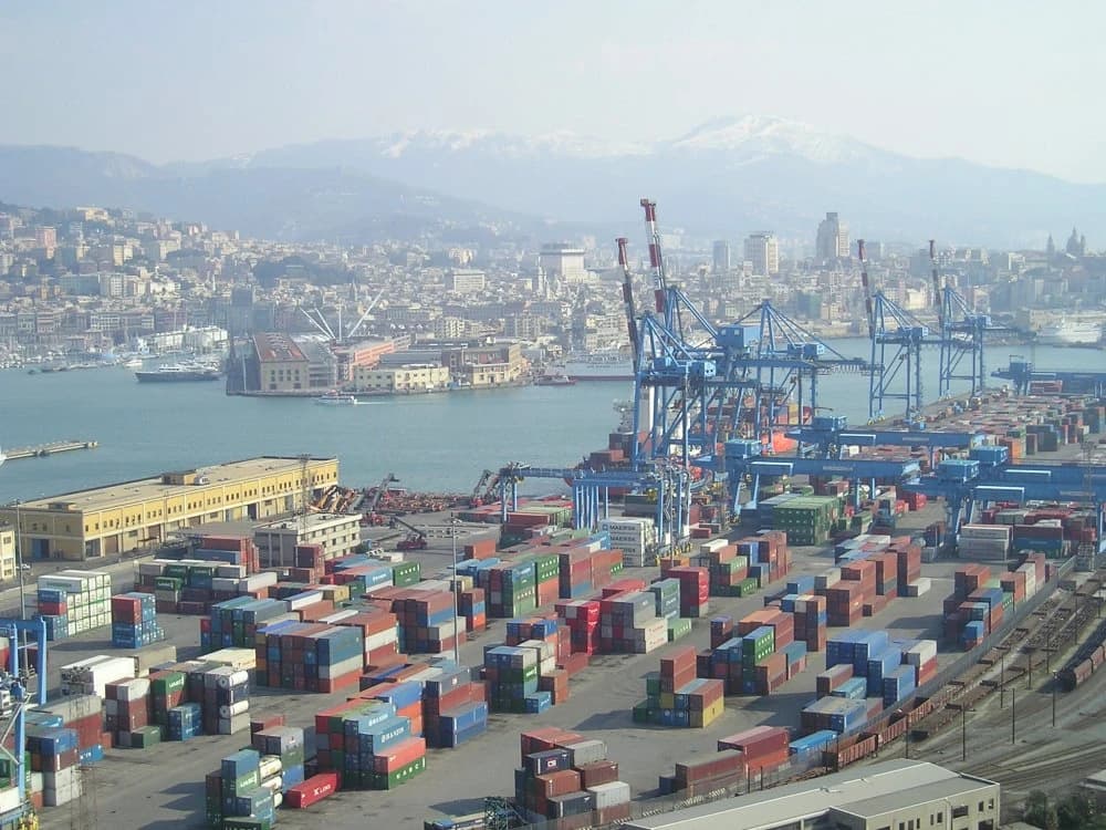 Aerial view of a bustling port with shipping containers, cranes, and city buildings.