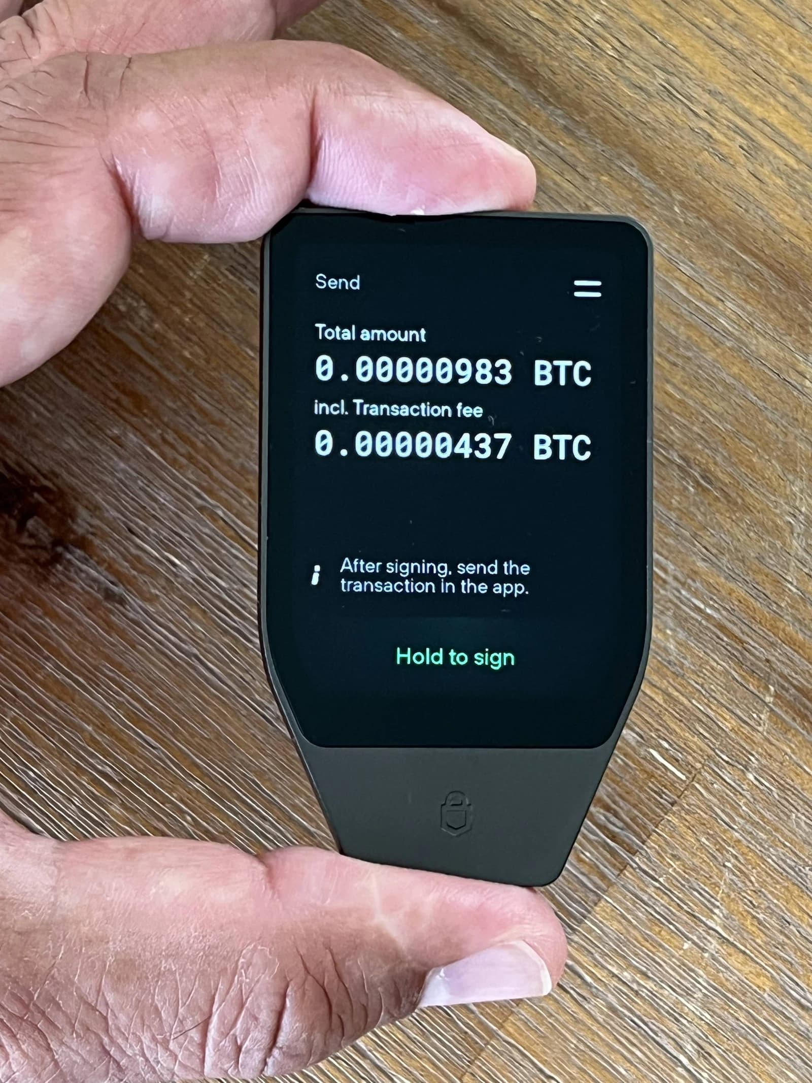 Hand holding a Trezor Safe T hardware wallet displaying a Bitcoin transaction.