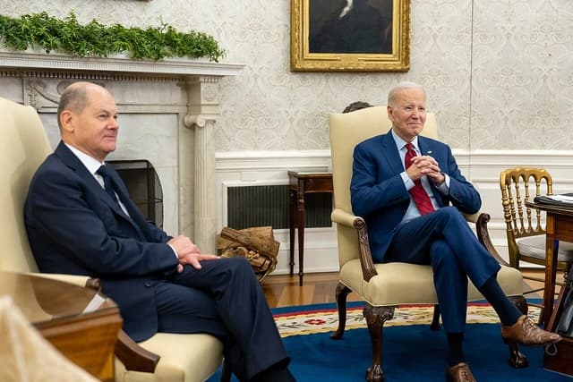 President Joe Biden sits with German Chancellor Olaf Scholz in a formal room.