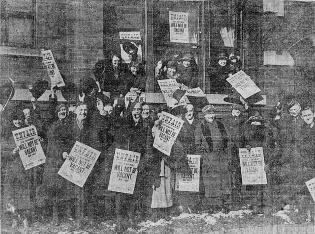 Group of protestors holding signs, some visible through a window, in an older black and white photograph.