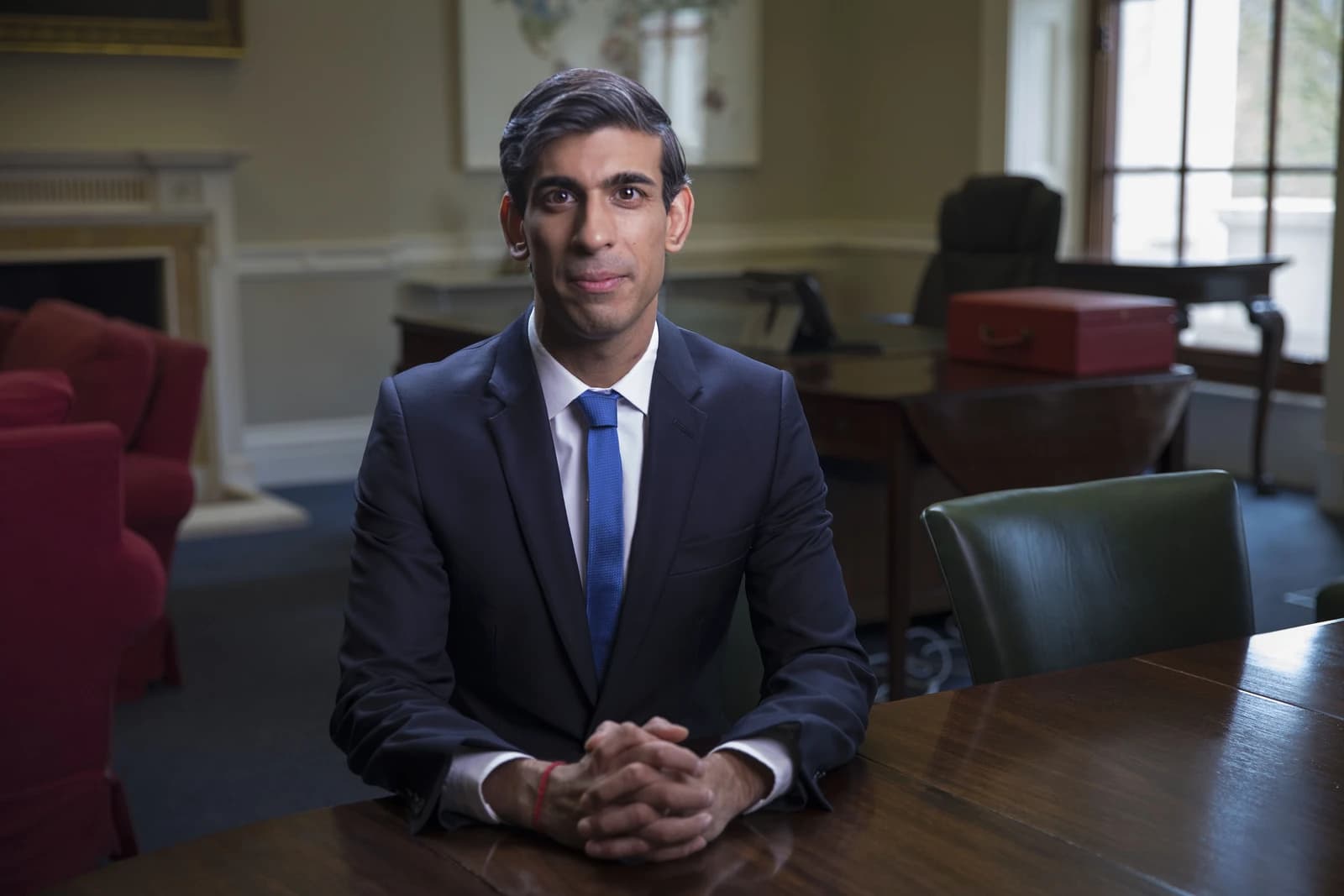 Rishi Sunak, former Chancellor of the Exchequer, sitting at a wooden desk with hands clasped.