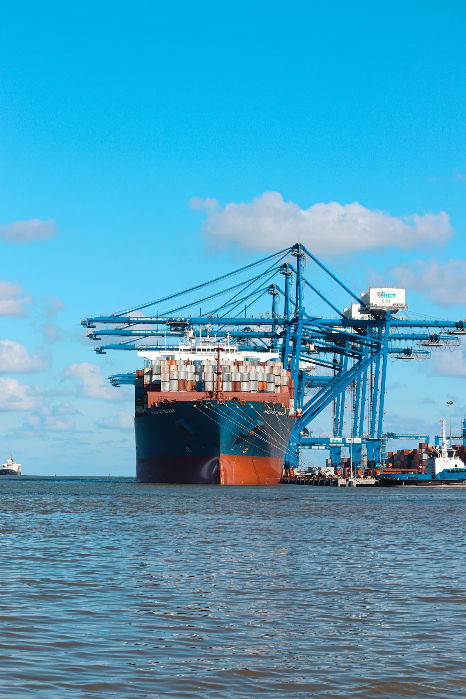 Container ship docked at Hai Phong International Container Terminal with blue gantry cranes.