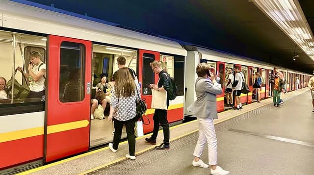 People boarding and disembarking a metro train at a station platform in Warsaw.