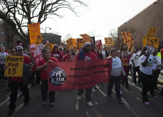 People holding signs and a large banner during a protest march on a street.