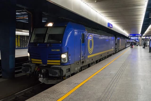 Blue and yellow X4 E-800 Vectron locomotive at a train station platform.