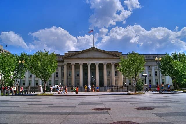 US Treasury Building, a large white neoclassical structure, under a blue sky.