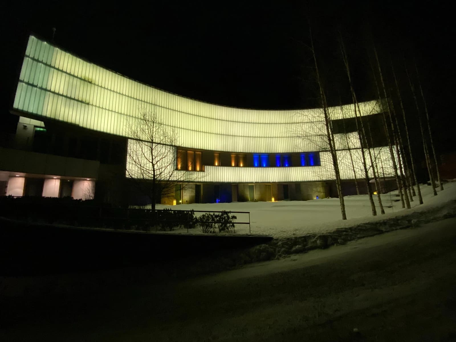 US Embassy Helsinki main building illuminated at night in blue and yellow colors.