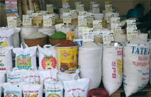 Bags and baskets of rice, some with price tags, displayed at a market stall.