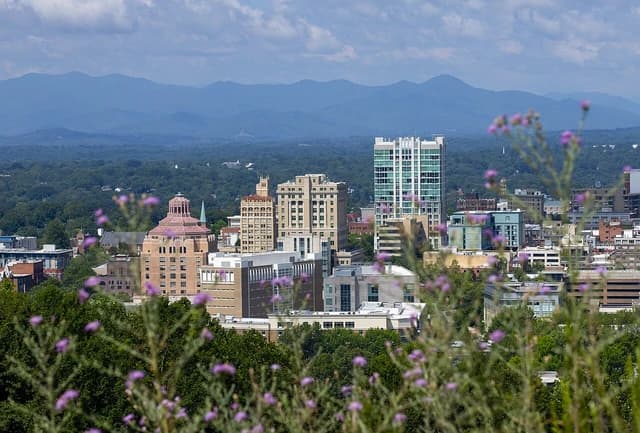 Downtown Asheville skyline with various buildings and Blue Ridge Mountains in the distance.