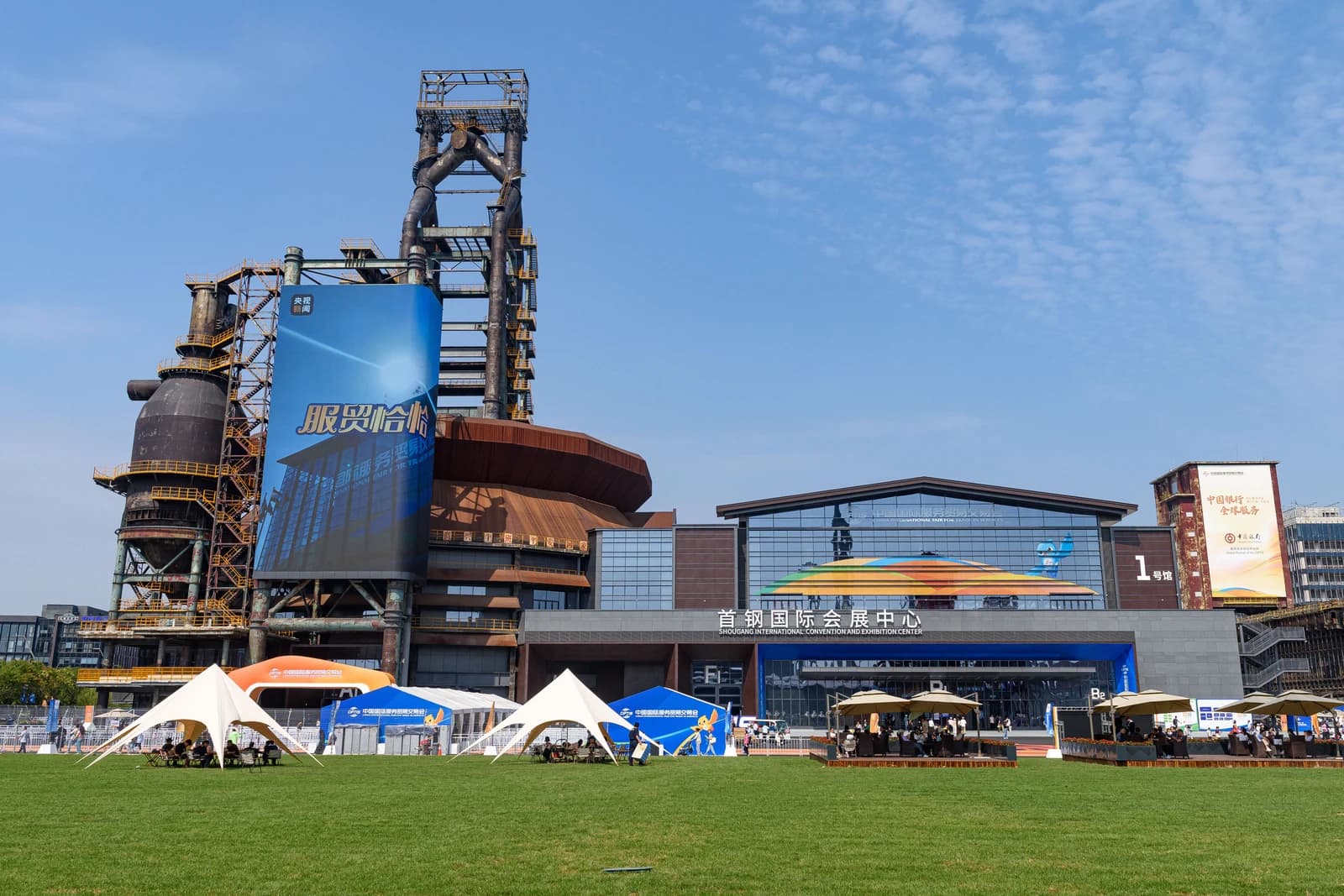 Shougang International Convention and Exhibition Center building with tents on a green lawn in front.
