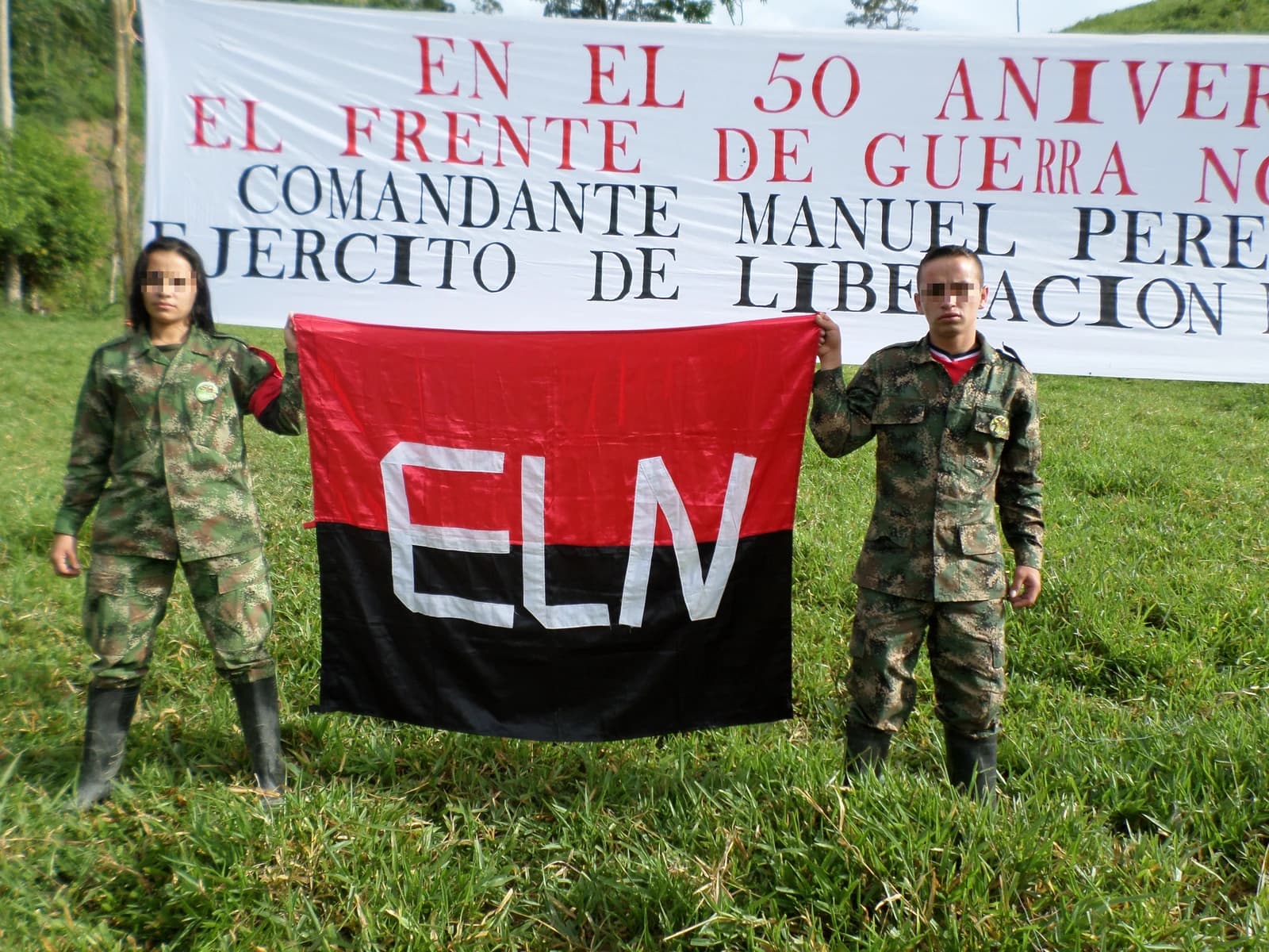 Two people in military camouflage uniforms hold up a red and black flag with ELN written on it.