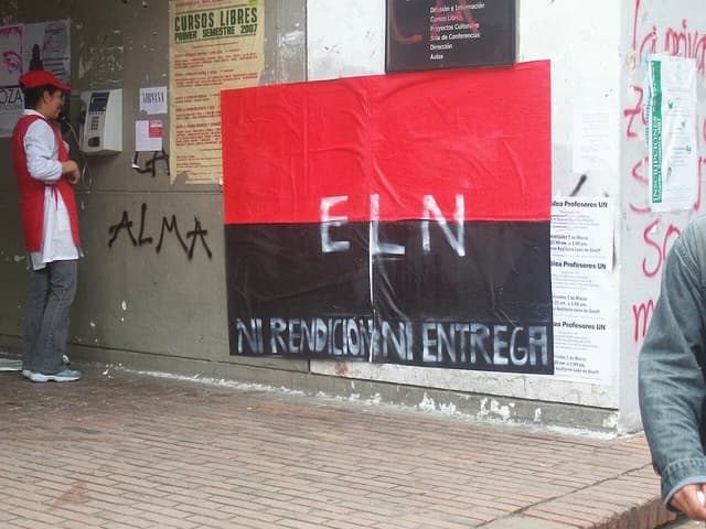 ELN guerrilla poster with text 'NI RENDICION NI ENTREGA' on a wall with other notices.
