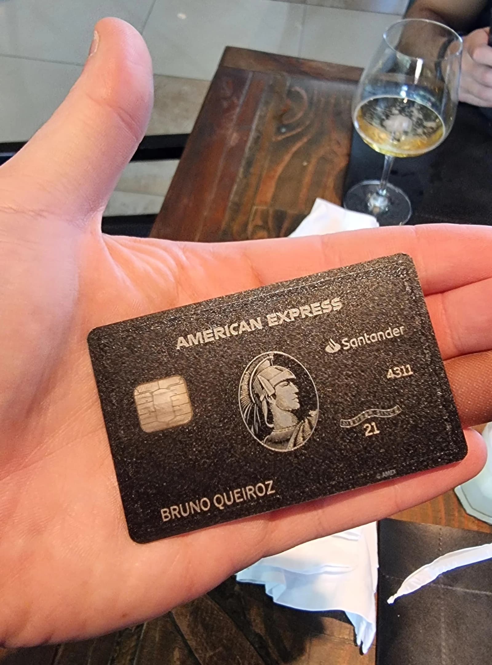 Hand holds an American Express Black card, showing card details and brand logos.