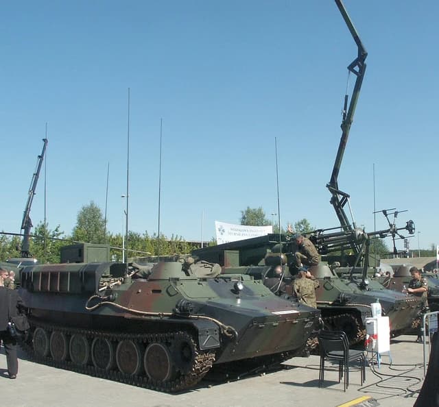 Military tracked vehicles, identified as MTLB Przebisnieg, with extended antennae and jammers.