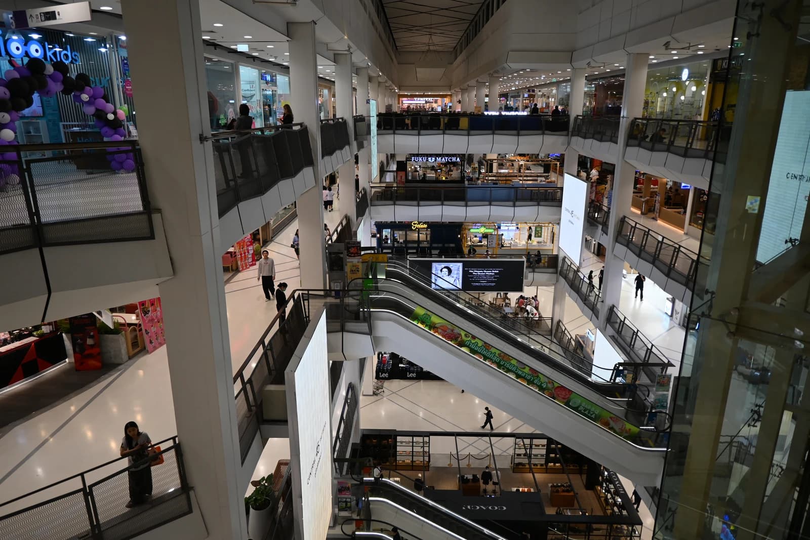Interior view of a multi-level shopping mall with glass railings and shoppers moving between floors.